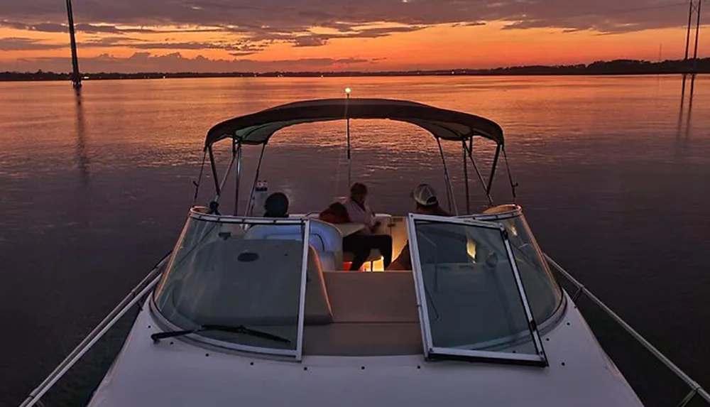 Two people are enjoying a sunset while sitting at the stern of a boat on calm waters