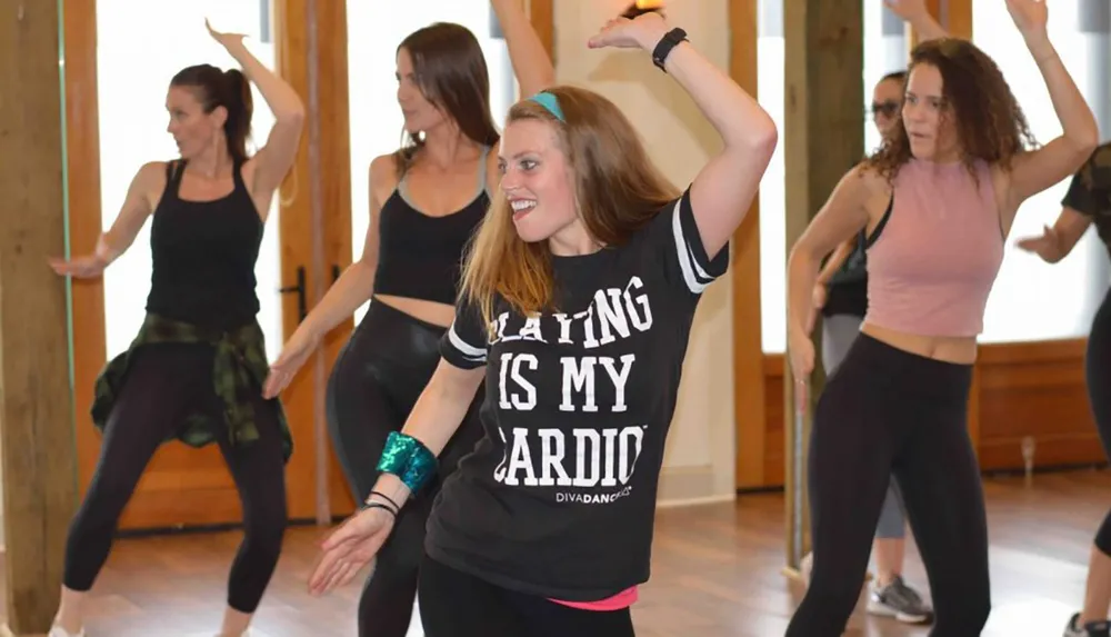 A group of people are participating in what appears to be a dance fitness class smiling and performing choreographed movements