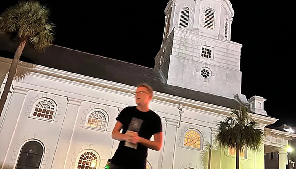 A person is blurred in motion in front of a well-lit historic building at night with a palm tree visible to the left