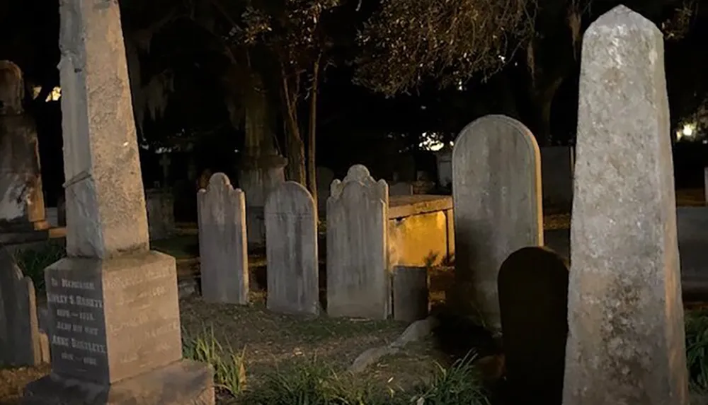The image shows a somber scene of a cemetery at night with various gravestones illuminated by ambient light