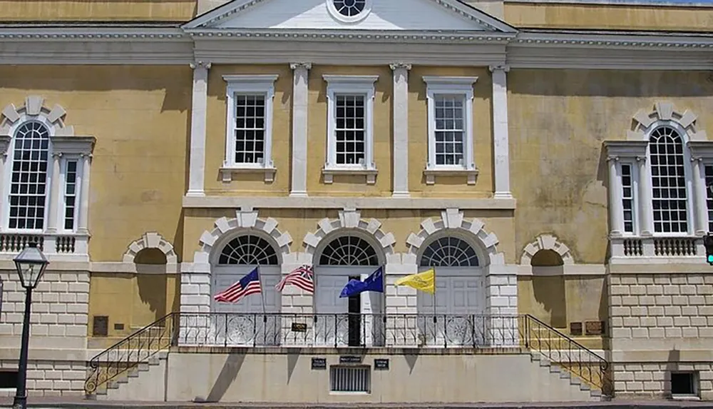 The image shows the facade of a historic yellow building with multiple flags including the American flag displayed in front