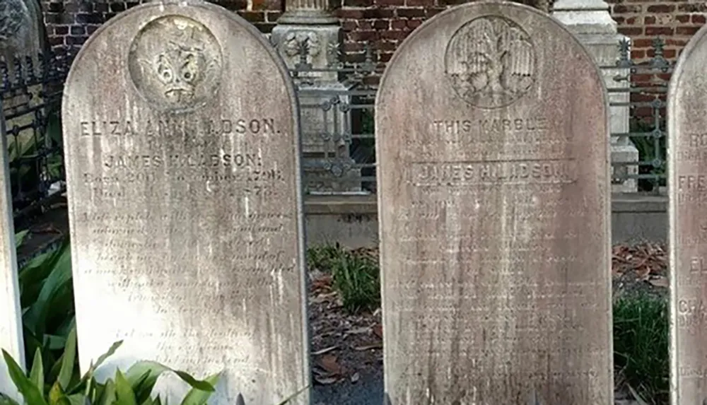 The image shows weathered gravestones with inscriptions each topped by a carving one of which appears to feature an owl and the other a floral motif