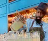 A bartender in a hat and apron is pouring a cocktail from a mixing jug into glasses lined up on a bar counter