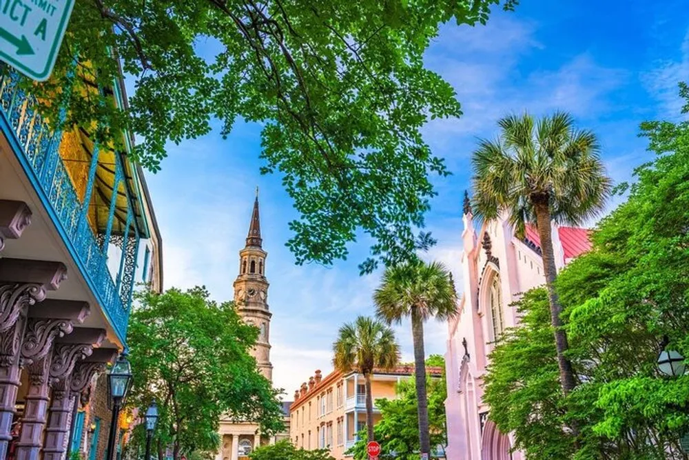 The image shows a picturesque street lined with colorful buildings a church spire palm trees and lush greenery under a bright blue sky