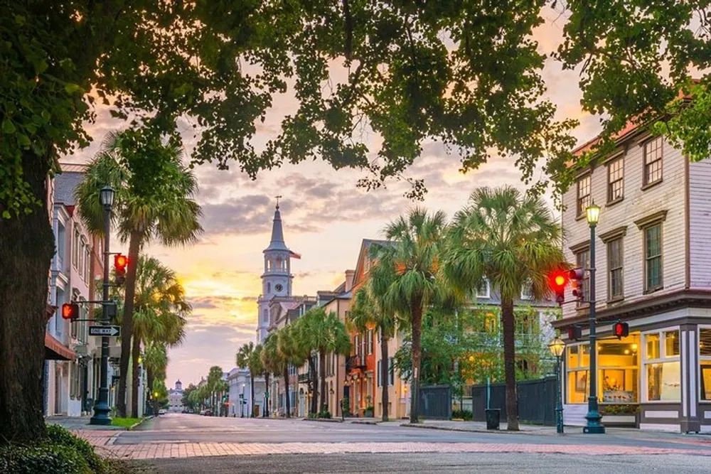 A serene sunset casts warm hues over a charming tree-lined street with historic architecture and a prominent church steeple in the background