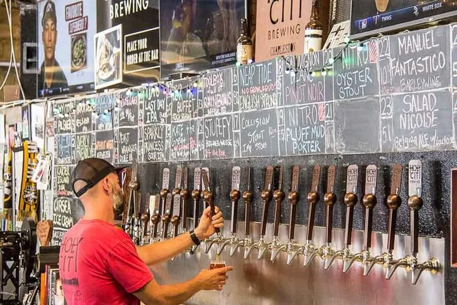 A person is selecting a beer tap from a row of options at a bar with a chalkboard menu listing a variety of craft beers.
