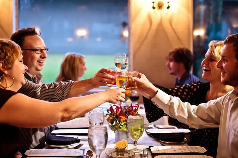 A group of people is joyfully toasting with drinks at a well-set table in a restaurant with a cozy ambiance