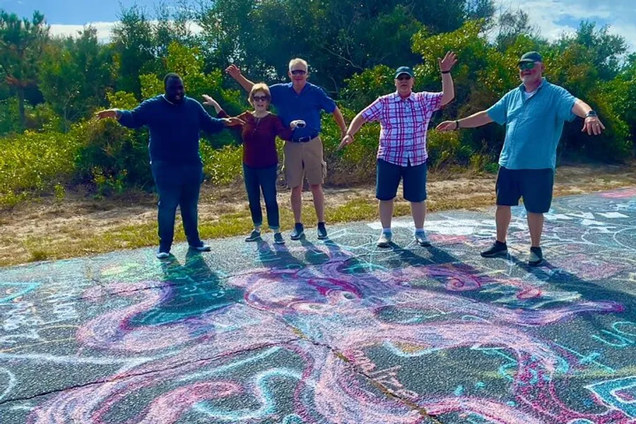 Five individuals are standing with their arms spread out on a pavement decorated with colorful chalk drawings, under a clear sky.