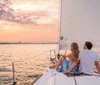 A couple is sitting on the deck of a sailboat enjoying a serene sunset over the water