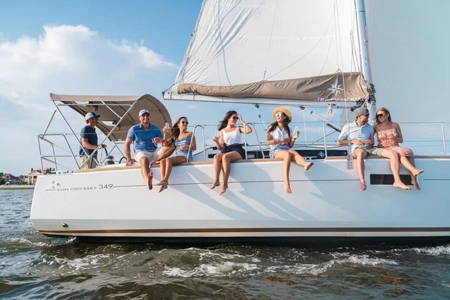 A group of people are enjoying a sunny day sailing on a yacht with their drinks in hand.