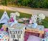 The image shows a cozy outdoor picnic setup with a low table comfortable cushions a basket and decorative elements including a sign that says Picnic with Puppies