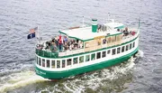 A group of passengers is enjoying a scenic boat tour on a green and white riverboat flying the American flag.