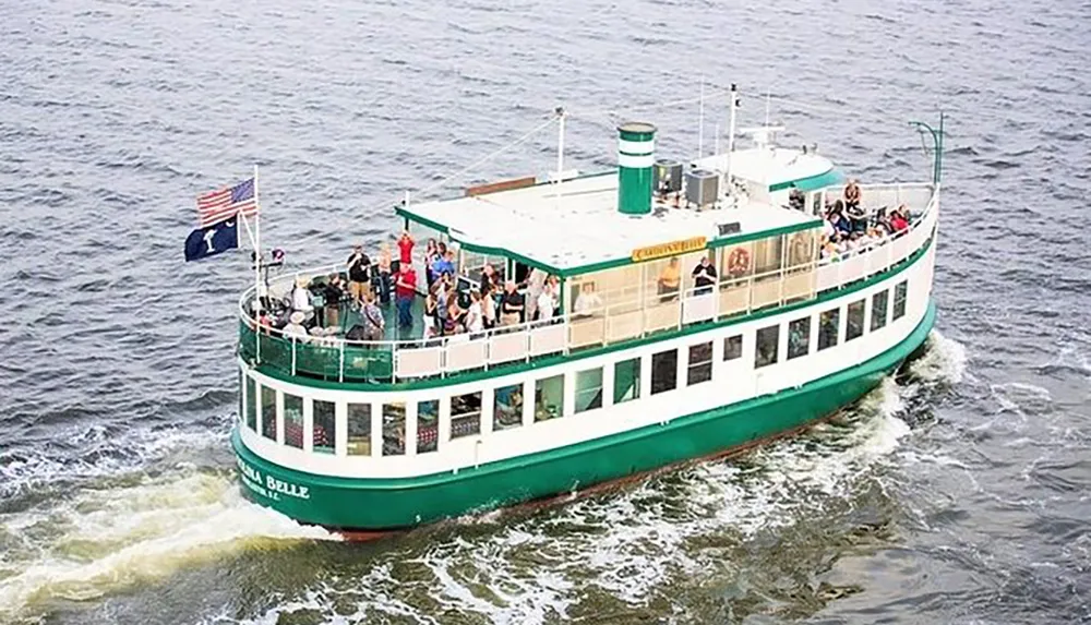 A group of passengers is enjoying a scenic boat tour on a green and white riverboat flying the American flag
