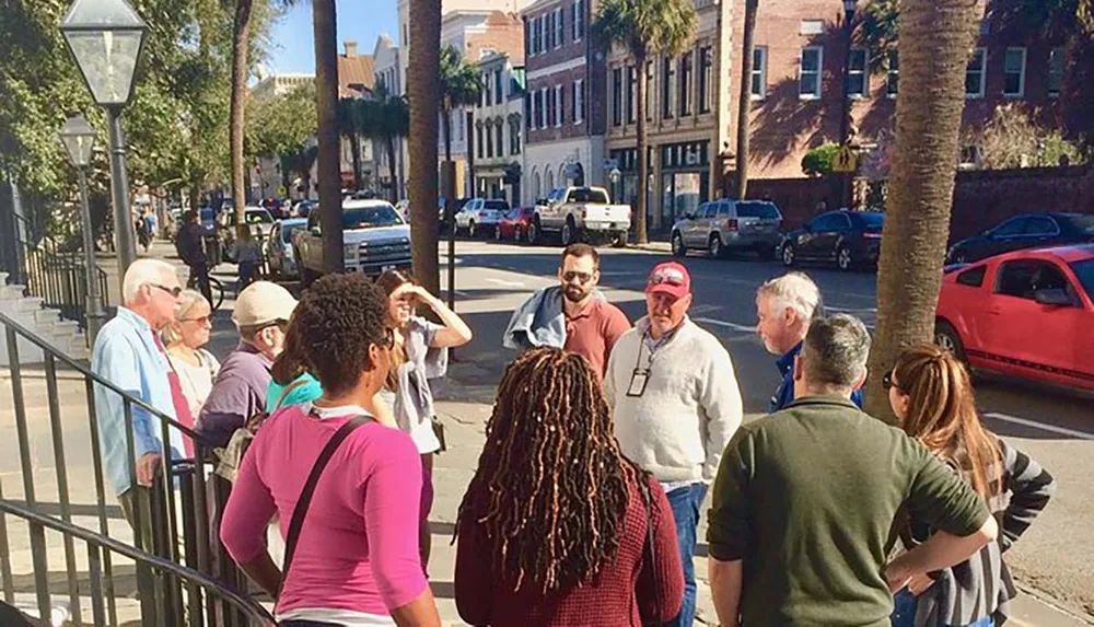 A group of people is engaged in what appears to be a guided tour on a sunny street lined with palm trees and historic buildings