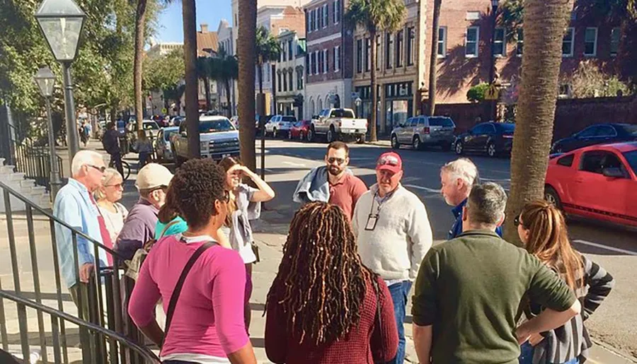 A group of people is engaged in what appears to be a guided tour on a sunny street lined with palm trees and historic buildings.