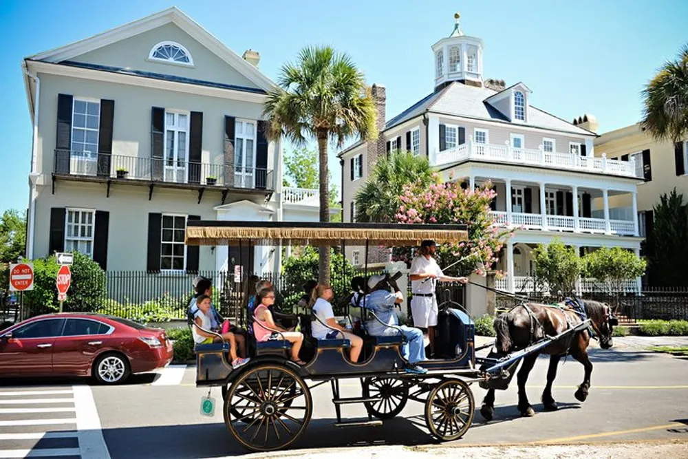 A horse-drawn carriage with passengers travels down a sunny street lined with historic houses
