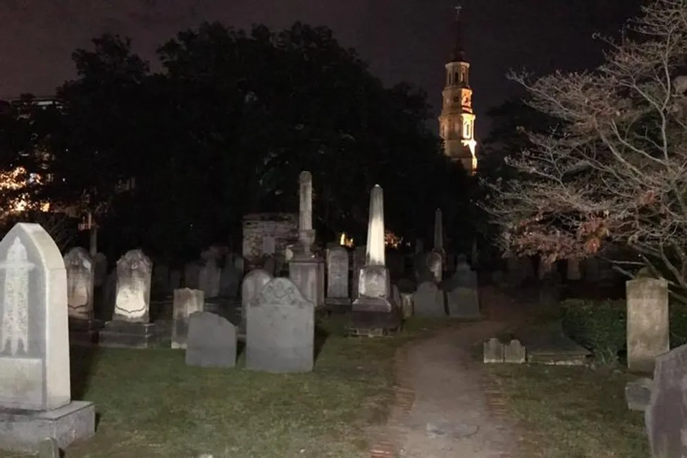 The image features a night scene of a graveyard with numerous headstones and a dimly lit church tower in the background