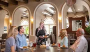 A group of four people is enjoying a meal in an elegantly designed dining area while a server brings additional dishes to the table.