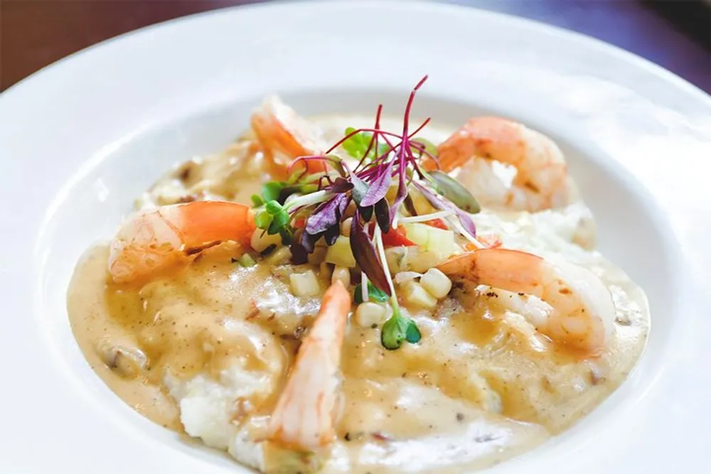 The image shows a gourmet dish consisting of shrimp atop a creamy bed of risotto or a similar grain garnished with microgreens served on a white plate