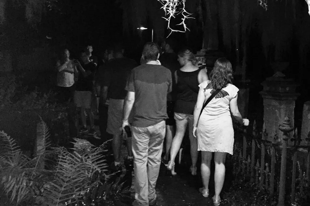A group of people is walking through what looks like a dimly lit outdoor area at nighttime with an eerie possibly historical ambiance