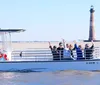 A group of people is joyfully waving from a boat with a lighthouse in the background