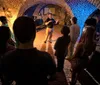 A group of people is attentively listening to a guide who is speaking and gesturing during a tour in an illuminated brick tunnel