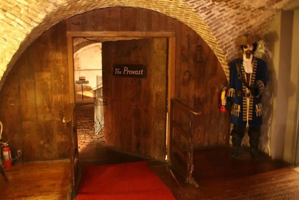 The image shows an old wooden door labeled The Provost set into a brick archway with a life-sized figure in historical military-style uniform standing nearby