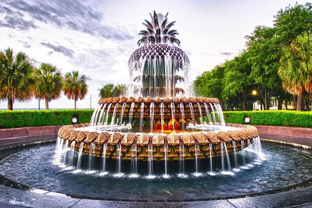 The image shows a large intricately designed pineapple-shaped fountain with water cascading over multiple tiers set against a background of palm trees and a blue sky with light clouds