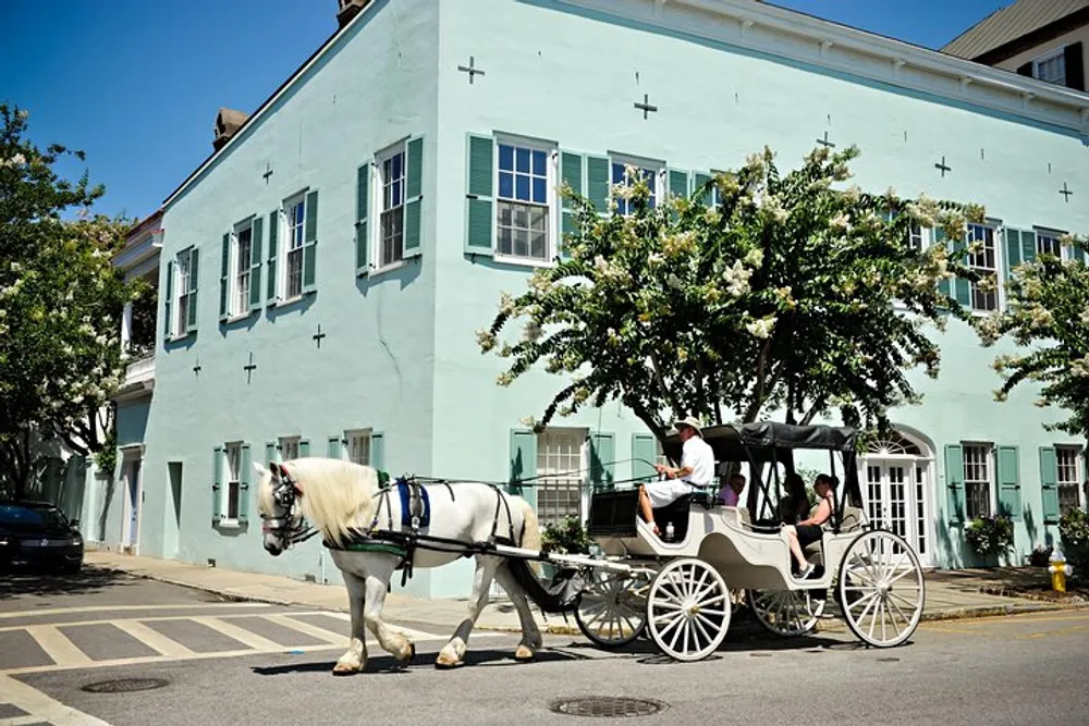 A horse-drawn carriage with passengers is trotting past a mint-green building on a sunny day with clear blue skies
