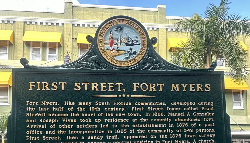 The image shows an informational sign about the history of First Street in Fort Myers Florida with a background of a building with yellow accents