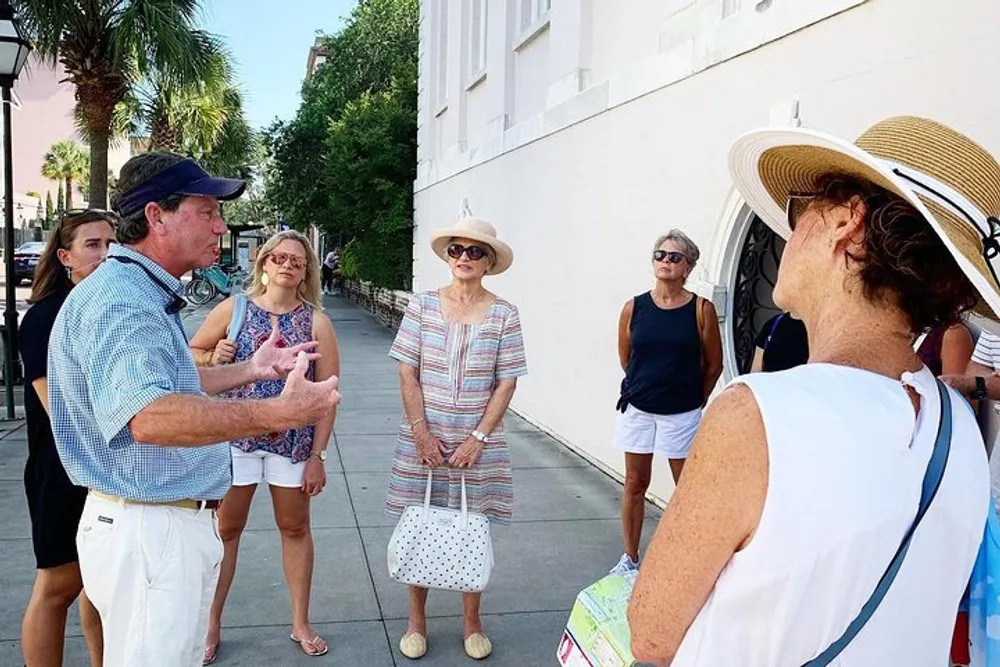 A group of people appear to be on a walking tour listening attentively to a guide who is speaking and gesturing with his hands
