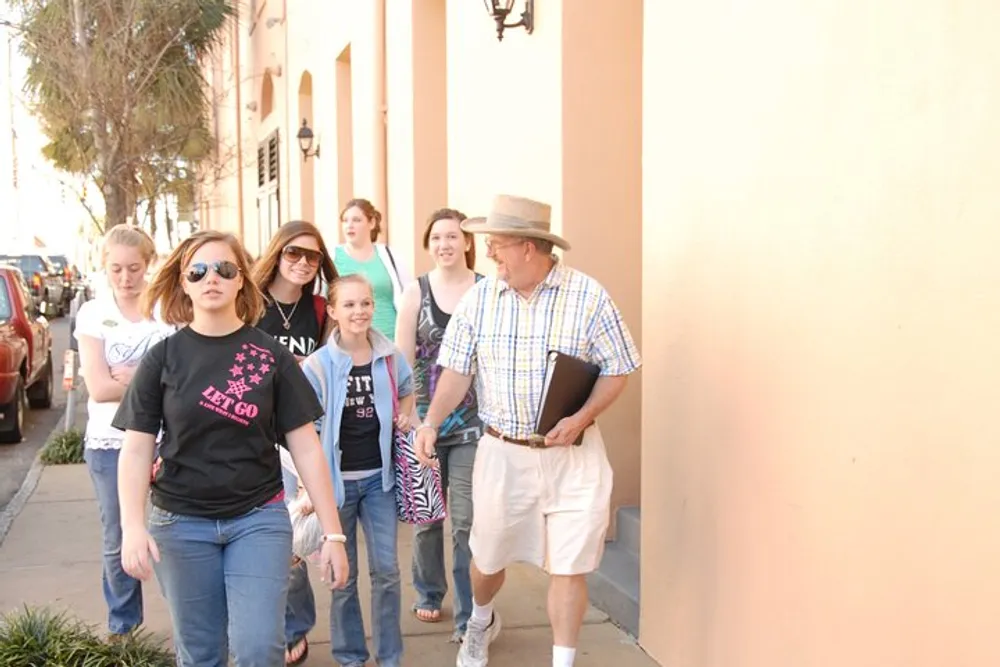 A group of people possibly led by a tour guide walking down a sunny sidewalk in an urban area