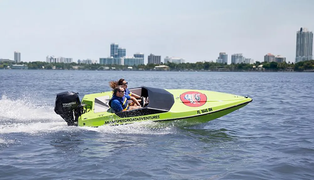 Two individuals are riding in a bright green speedboat on a body of water with a city skyline in the background