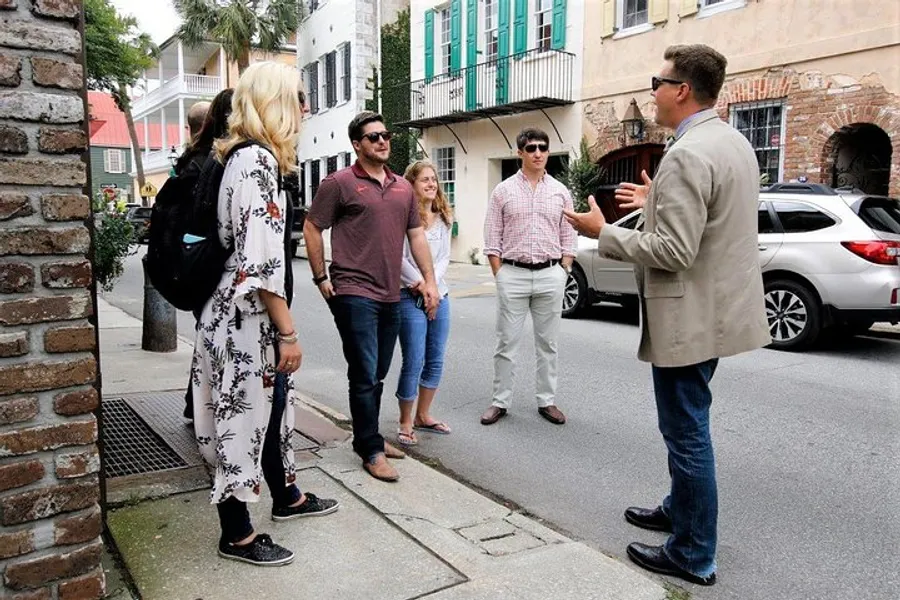 A group of people is listening to a man who appears to be giving a tour on a city street.