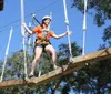 A person wearing a helmet and safety harness is navigating a high ropes course among trees under a clear blue sky