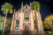 A Gothic-style church is illuminated at night, framed by palm trees under a starry sky.