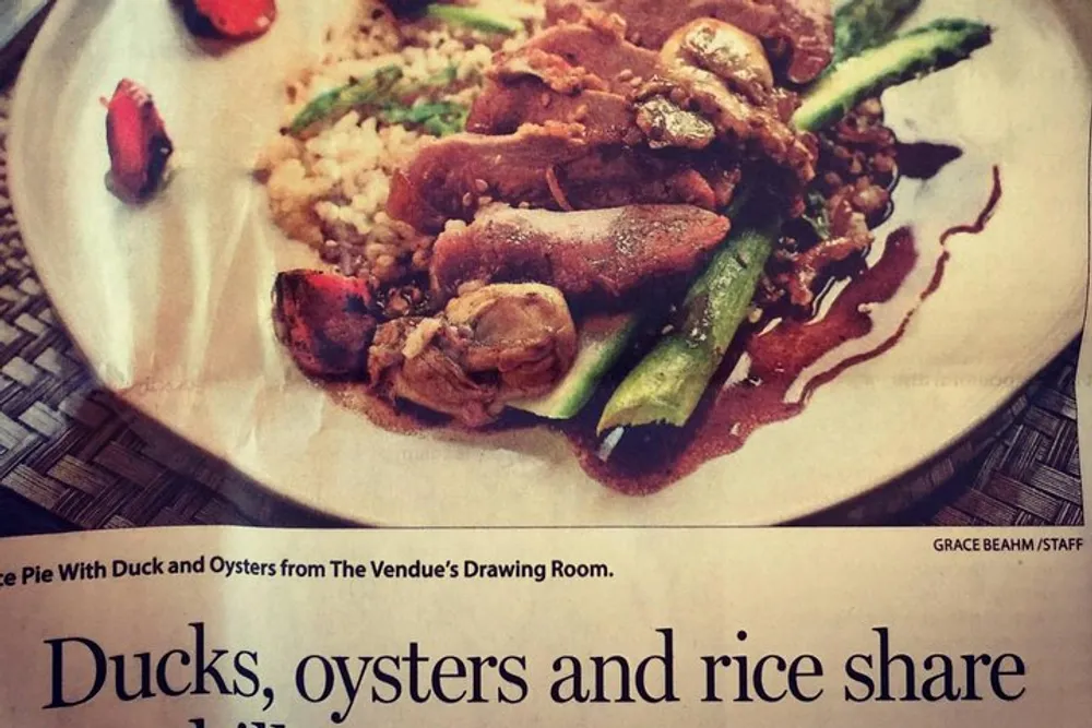The image shows a printed photograph of a plate containing a dish with duck oysters and rice garnished with green vegetables with partially visible text that describes a culinary article