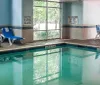 An indoor swimming pool with blue lounge chairs safety signs and a depth marker of 4 feet 10 inches flanked by windows that let in natural light
