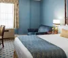 The image shows an elegantly furnished hotel room with a queen-sized bed blue walls patterned curtains and classic-styled furniture