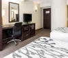 The image shows a neatly arranged hotel room with a green accent wall artistic black and white photographs and a bed with a decorative floral bedspread
