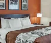 The image shows a neatly made hotel room with a large bed crisp white bedding a floral patterned throw and warm-toned walls flanked by artwork and modern lighting