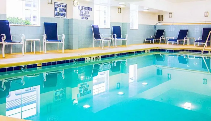 An indoor swimming pool with blue lounge chairs on the deck and safety signs indicating No Diving Allowed and Swim at Your Own Risk