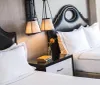 This image depicts a neatly arranged hotel room with two beds stylish headboards elegant hanging bedside lamps crisp white linens and a nightstand with a small flower vase and books