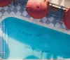 The image shows an aerial view of a swimming pool with the phrase A GOOD TIME STATE OF MIND written on the bottom flanked by red umbrellas and a patterned deck