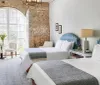 The image shows a bright and cozy twin bedroom with exposed brick walls arched windows with shutters and stylish decor