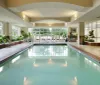 The image shows an indoor swimming pool area with lounge chairs and large windows letting in natural light