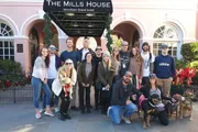 A group of smiling people, some with dogs, are posing for a photo in front of The Mills House Wyndham Grand Hotel.