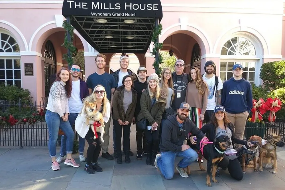A group of smiling people some with dogs are posing for a photo in front of The Mills House Wyndham Grand Hotel
