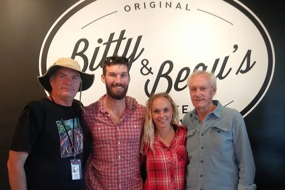 Four people are smiling for a photo in front of a sign that reads Bitty  Beaus Original