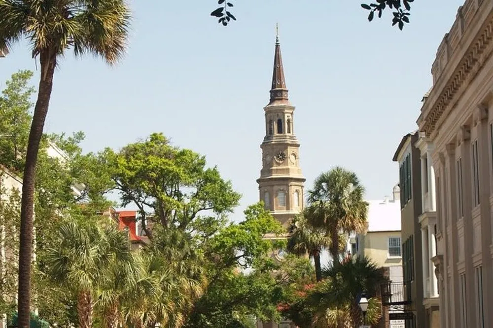 The photograph captures a charming urban street lined with historical buildings and lush greenery with a striking church steeple rising prominently in the background under a clear sky